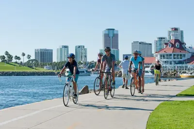 a group of people riding bikes on a sidewalk by the water at People's Choice Central Location Prkg & Patio LBD in Long Beach