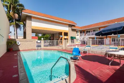 a swimming pool in front of a hotel with a table and umbrella at Rodeway Inn Artesia Cerritos in Artesia