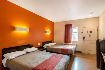 a hotel room with two beds with orange walls at Motel 6 Bell Gardens, CA - Los Angeles in Bell Gardens