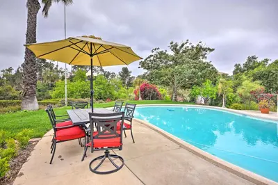 a table and chairs with an umbrella next to a swimming pool at The Castle Hacienda Heights Home with Patio and Pool in Hacienda Heights