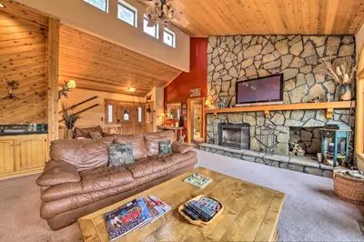 a living room with a leather couch and a stone fireplace at Hike, Ski, Fish Big Bear Lake Lodge with Deck in Big Bear Lake