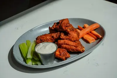 a plate of chicken wings and vegetables with a dipping sauce at Hilton Garden Inn Anaheim Resort in Anaheim