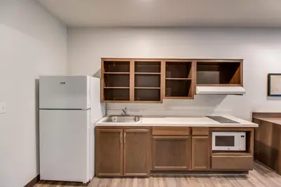 a kitchen with a white refrigerator and wooden cabinets at WoodSpring Suites Bakersfield Airport in Bakersfield