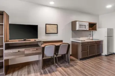 a room with a desk with a tv and a kitchen at WoodSpring Suites Bakersfield Airport in Bakersfield