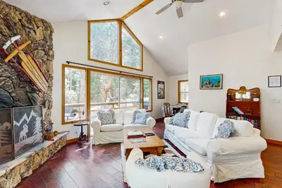 a living room with white furniture and a large stone fireplace at Babbling Brook in Lake Arrowhead
