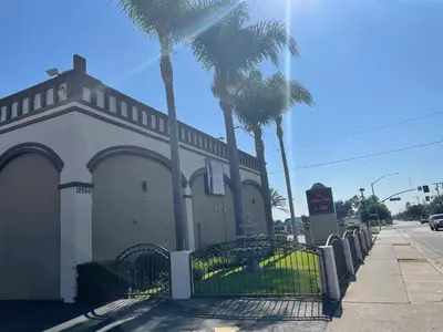 a building with a gate and palm trees on a street at Legacy inn & suites in Anaheim