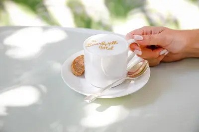 a person holding a cup of coffee on a table at The Beverly Hills Hotel - Dorchester Collection in Los Angeles