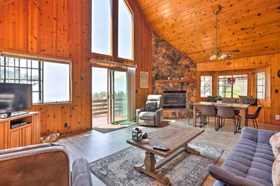 a living room with wood paneling and a tv and a table at A-Frame Cali Cabin with Unobstructed Valley Views! in Running Springs