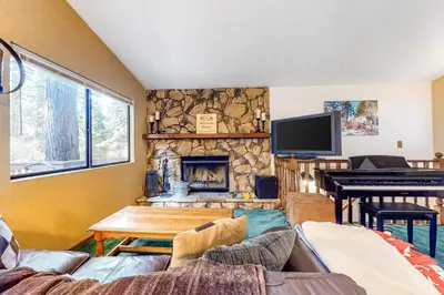 a living room with a stone fireplace and a piano at Morrison Manor in Lake Arrowhead