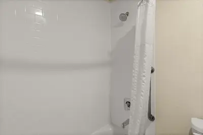 a shower with a white shower curtain in a bathroom at Good Nite Inn Buena Park in Buena Park