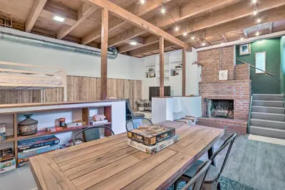 a room with a wooden table and a brick fireplace at Modern and Unique Cabin with Deck by Lake Gregory! in Crestline