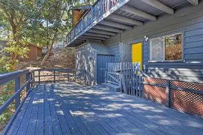 a blue house with a wooden deck and stairs at Modern and Unique Cabin with Deck by Lake Gregory! in Crestline