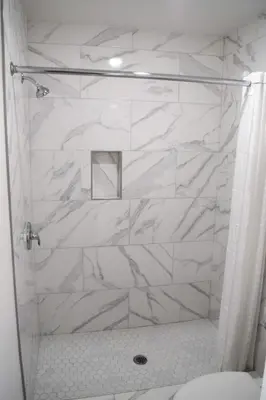 a bathroom with a shower with white marble walls at Mojave Inn in Victorville