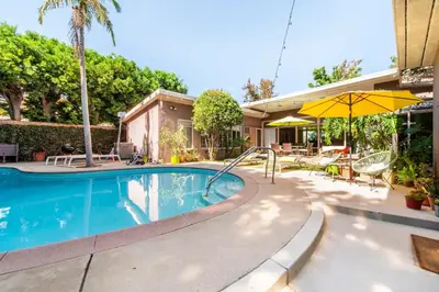 a swimming pool with an umbrella next to a house at Bixby Beauty 50s Mod Long Beach in Long Beach