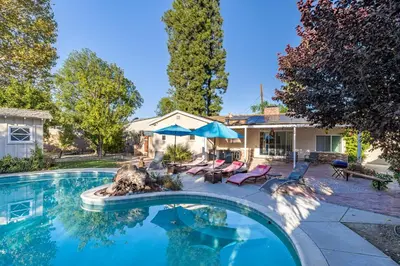 a swimming pool with chairs and umbrellas next to a house at Spacious Home with Garden & Pool in Northridge
