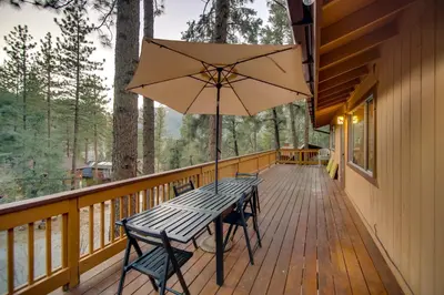 a wooden deck with a picnic table and an umbrella at Peaceful and Idyllic Forest Cabin with Pool Table in Pine Mountain Club
