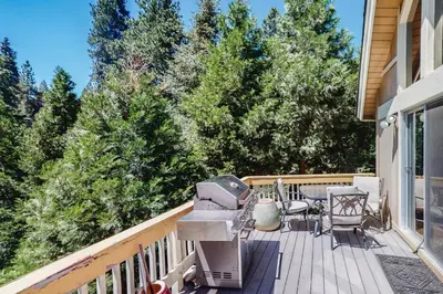 a deck with a grill and chairs and trees at Dragon's Lair in Lake Arrowhead