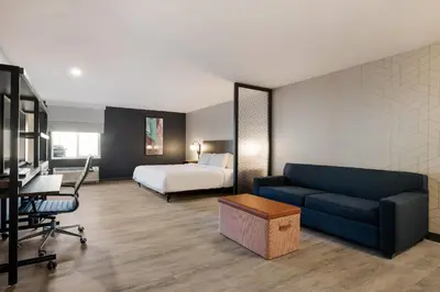 a hotel room with a bed and a couch and a desk at Everhome Suites Corona in Corona