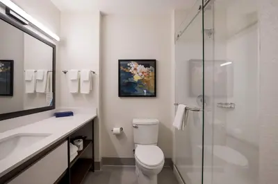 a bathroom with a toilet and a glass shower at Everhome Suites Corona in Corona