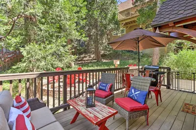 a deck with chairs and tables and an umbrella at Steps to Lake Cabin with Deck in Lake Arrowhead in Lake Arrowhead