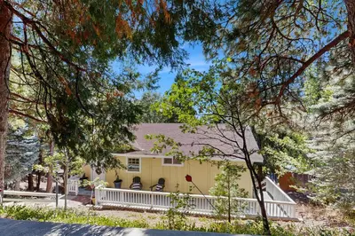 a yellow house with a white fence and trees at Treetop Cottage in Running Springs