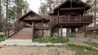 a log cabin with a porch and stairs to it at Shoreline Lakehouse by AvantStay Majestic Lakefront Cabin w Hot Tub Fire Pit in Big Bear Lake