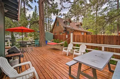 a wooden deck with chairs and a table and umbrella at 3 Mi to Skiing Big Bear Cabin with Deck in Big Bear City