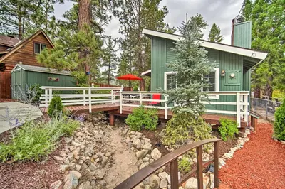 a green house with a white fence in front of a yard at 3 Mi to Skiing Big Bear Cabin with Deck in Big Bear City