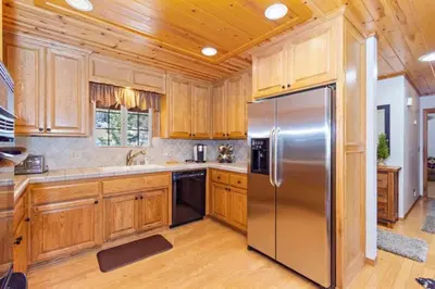 a kitchen with wooden cabinets and a stainless steel refrigerator at CUSTOM SINGLE STORY CABIN WITH JACUZZI POOL TABLE & BIG GAME ROOM WITH ARCADE games in Big Bear Lake