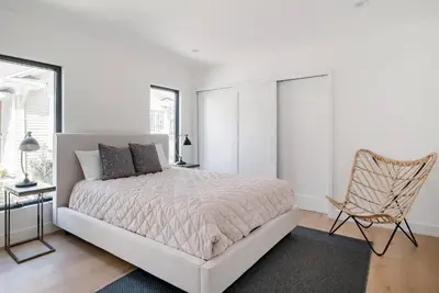a white bedroom with a bed and a chair at Modern Bungalow with a Pool in Larchmont Village in Los Angeles