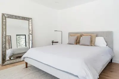 a white bedroom with a large bed and a mirror at Modern Bungalow with a Pool in Larchmont Village in Los Angeles