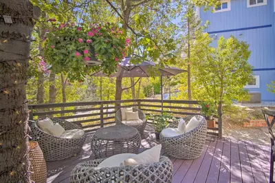 a deck with chairs and tables and an umbrella at Chic Lake House with Furnished Deck and Hot Tub! in Lake Arrowhead