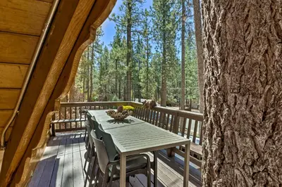 a table on the deck of a cabin with a tree at Modern Cabin with Hot Tub Ski and Hike Big Bear! in Big Bear Lake