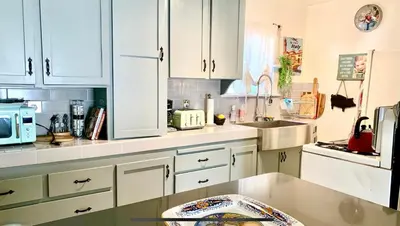 a kitchen with white cabinets and a sink at Romantic cottage with amazing garden in Glendale