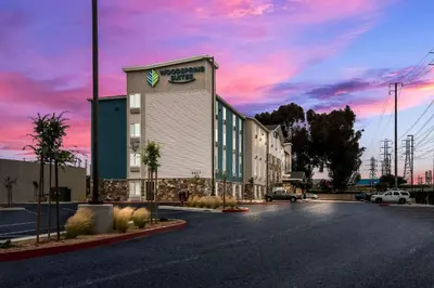 a building on the side of a street with a sunset at WoodSpring Suites Bellflower - Los Angeles in Bellflower