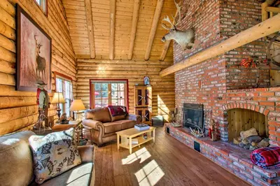 a living room with a brick fireplace in a log cabin at Pine Mountain Club Log Home with Deck and Grill! in Pine Mountain Club