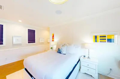 a white bedroom with a large bed and a lamp at Gull Cottage in Seal Beach
