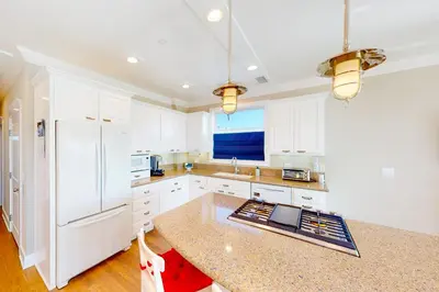 a kitchen with white cabinets and a white refrigerator at Gull Cottage in Seal Beach