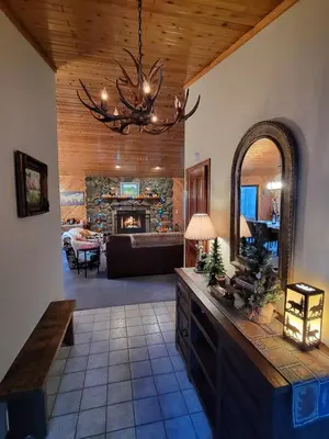 a living room with a stone fireplace and a chandelier at Four Seasons Getaway-Private Hot Spa with Pine Tree Views-Walk to Village and Pineknot Trailhead-Plus King Bed! in Big Bear Lake