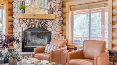 a living room with two chairs and a stone fireplace at Tanglewood by AvantStay 10mins to Bear Mountain Contemporary Hillside Cabin in Big Bear Lake