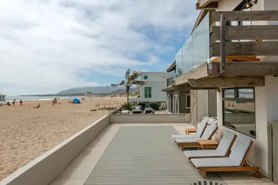 a building on the beach with chairs and people on the beach at Luxury Modern Designer Beach House on Sand w/ Pool in Ventura
