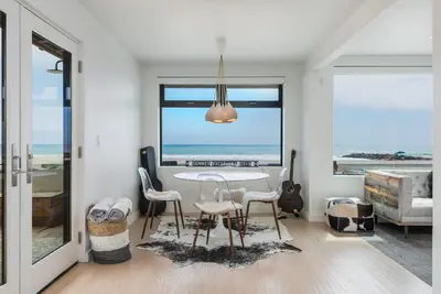 a dining room with a table and chairs and the ocean at Luxury Modern Designer Beach House on Sand w/ Pool in Ventura