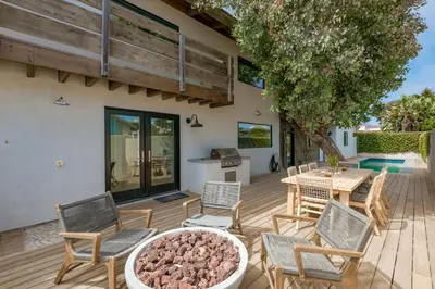 a patio with a table and chairs and a wooden deck at Luxury Modern Designer Beach House on Sand w/ Pool in Ventura