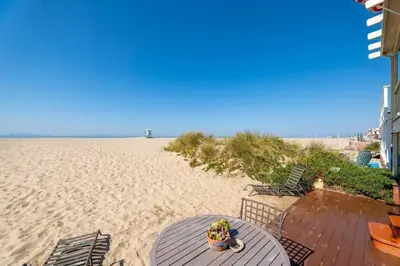 a table and chairs on the beach near the sand at Beautiful Ocean Front Coastal Sunset Beach House in Oxnard