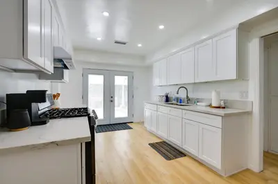 a white kitchen with white cabinets and a wooden floor at Home Between Los Angeles and Disney! Patio, Yard in Pico Rivera