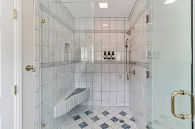 a white tiled bathroom with a shower with a bench at The Big Sky in Pearblossom