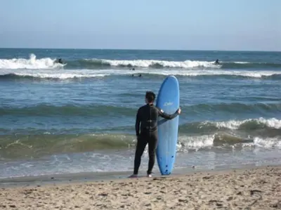 a man standing on the beach holding a blue surfboard at 30 PCT OFF! Malibu Peaceful Getaway, Beach, Ocean in Malibu
